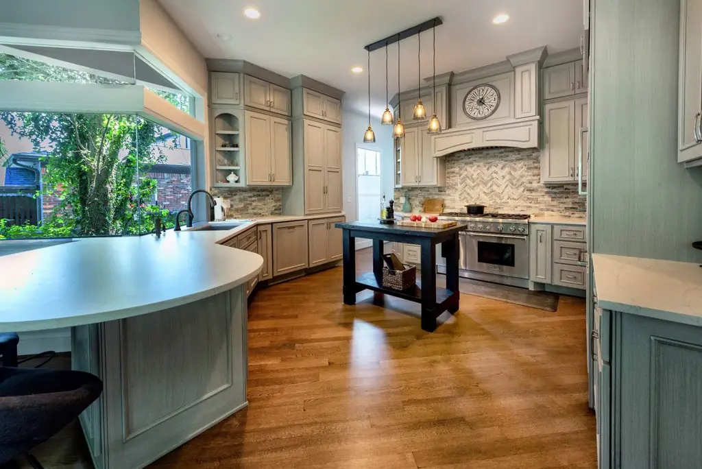 A remodelled kitchen with grey-green cabinetry, herringbone backsplash and a black butcher-block island